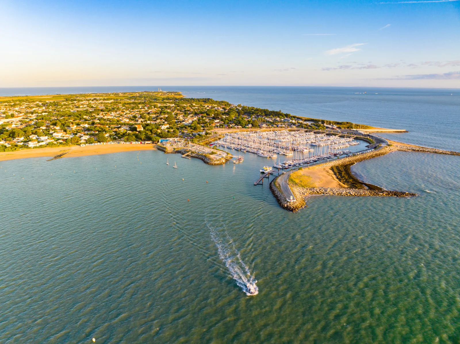 Vue aérienne du port de Saint-Denis-d'Oléron, un bateau à moteur à l'entrée du chenal, le phare de Chassiron au loin